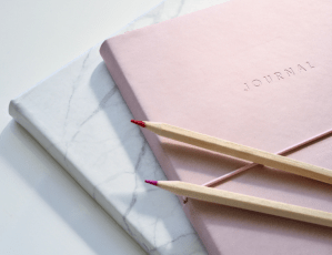 Photo of pink journal with two pencils on top.